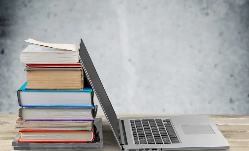 Open laptop up against a stack of books