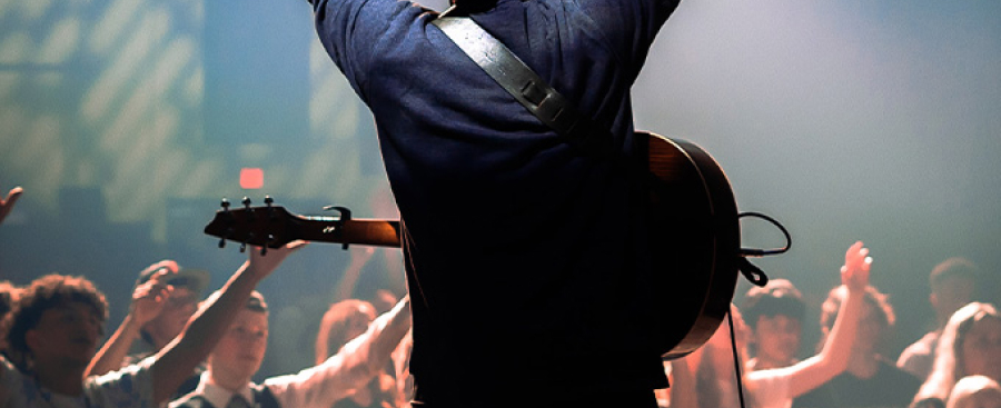 Man on stage with a guitar leading musical worship