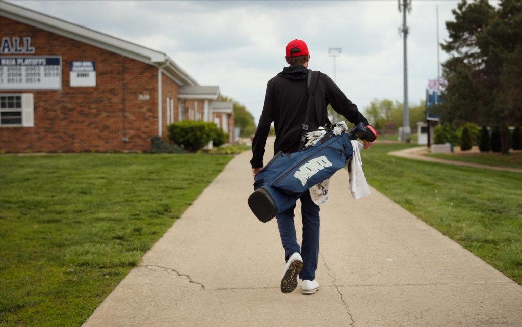 Student with golf clubs walking down a path