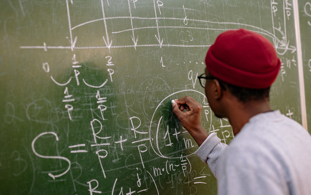 Student solving an equation on a blackboard