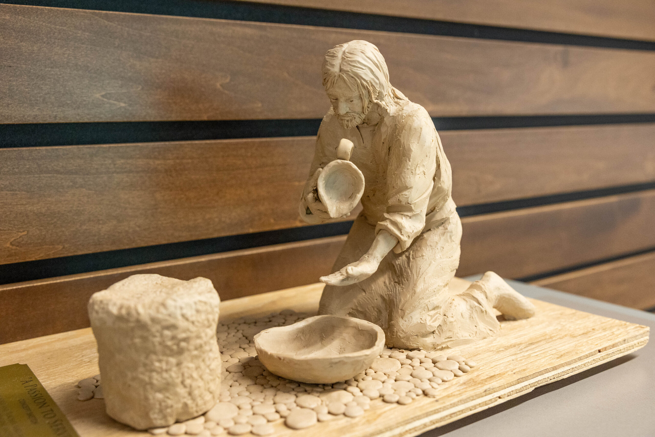 Passion to Serve sculpture rendering in clay. Figure kneeling, pouring water into a bowl